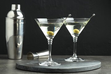 Martini cocktail with olives in glasses on grey table against black background
