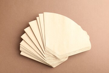 Paper coffee filters on brown background, top view