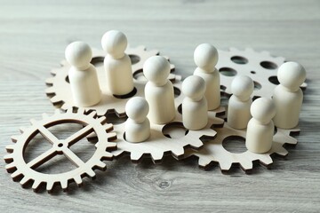 Human resources concept. Many figures and gearwheels on wooden table, closeup