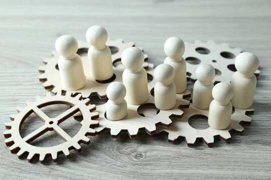 Human resources concept. Many figures and gearwheels on wooden table, closeup
