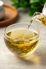A warm cup of green tea is being poured from a glass teapot into a transparent bowl, showcasing the tea leaves floating within, This image is perfect for wellness, beverage articles