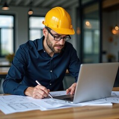 Engineer in yellow helmet works on construction drawing. Project manager uses laptop, papers. Man plans real estate. Focused on details for construction site. Attentive, immersed in project. Modern