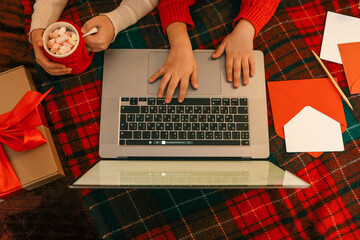 A group of children watching a video chat with Santa using a laptop in a decorated room during...