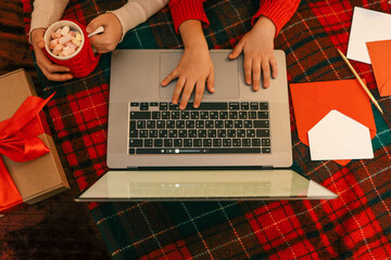 A group of children watching a video chat with Santa using a laptop in a decorated room during...