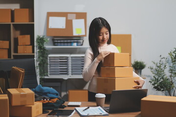 Startup SME small business entrepreneur of freelance Asian woman wearing apron using laptop and box to receive and review orders online to prepare to pack sell to customers, online sme business ideas.