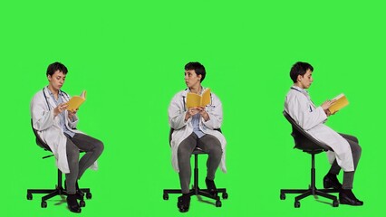 Obraz premium Medic specialist reading a medicine literature book sitting on a chair, enjoying healthcare industry lecture against greenscreen backdrop. Doctor in white coat reads for relaxation. Camera A.