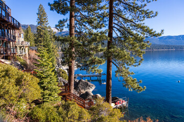 a gorgeous winter landscape at Lake Tahoe with blue lake water, lush green trees and plants and...
