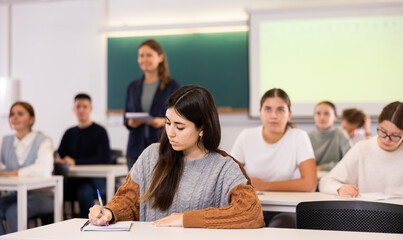 Female student sit at desk and makes notes in her textbook