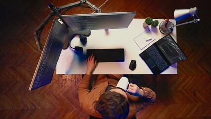 Top down view of self employed man doing IT support job from apartment personal office, coding on...