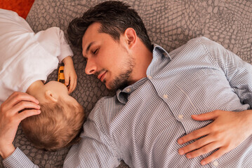 A young father shares love with his son and spends time together at home, lying and sleeping on the bed, top view. 