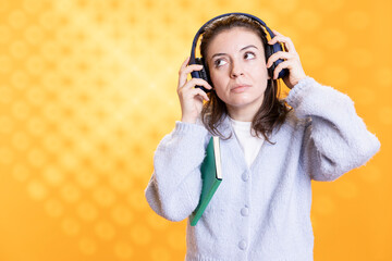 Woman holding book and listening music, conveying how fun reading is, studio background. Bookworm lady reading novel and hearing songs in headphones, promoting literature as entertainment