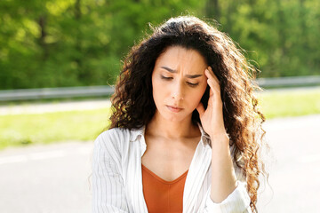 Young stressed woman standing on highway near broken car while her boyfriend calling breakdown road service on smartphone. Millennial multiracial couple having auto accident during travels