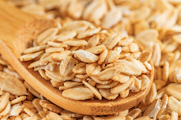 Rolled oats on a wooden spoon with blurred oats in the background. Ideal for healthy and organic food themes.