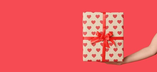 Female hand holding gift box on red background with space for text. Valentine's Day celebration