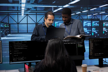 Diverse team of engineers in data center looking for firewall misconfigurations affecting servers. Multiracial workers in server room check systems bottlenecks leading to sluggish data transfer rates
