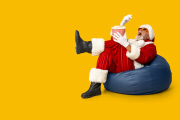 Santa Claus in 3D glasses eating tasty popcorn on yellow background