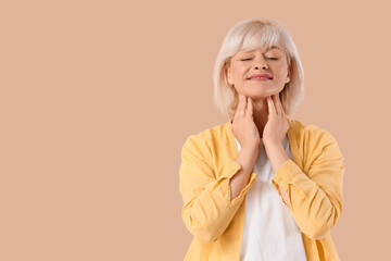Mature woman self-examining thyroid gland on beige background