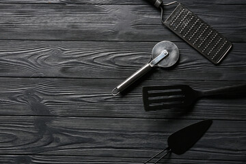 Set of different kitchen utensils with stainless steel pizza cutter on dark wooden background