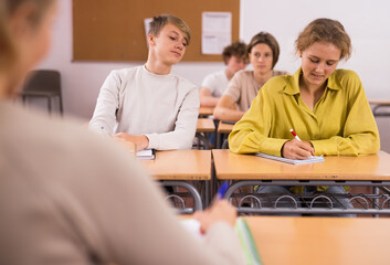 Teenage girl and boy sitting together at desk and doing tasks in classroom.