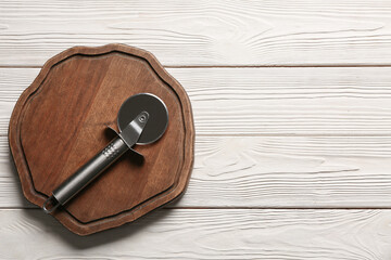 Board with stainless steel pizza cutter on light wooden background