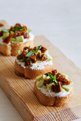 selective focus of italian bruschetta with dried tomatoes, avocado, cream cheese and herbs on wooden board, close up, vertical