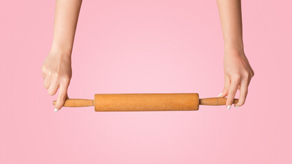 Home baking concept. Woman holding wooden rolling pin on pink background, closeup of hands. Panorama