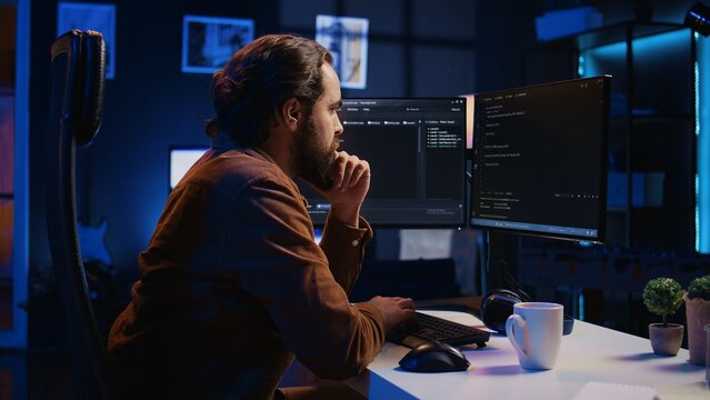 Programmer doing web development during remote job shift in neon lit home office, finishing coding project. IT specialist sitting at computer desk, working on desktop PC, camera B