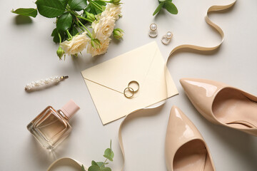 Wedding rings with envelope, flowers and bridal accessories on light background