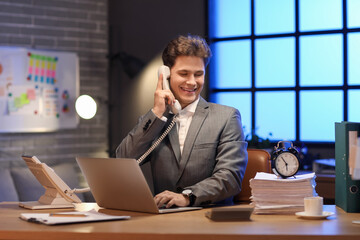 Happy businessman talking by telephone and meeting deadline in office at night