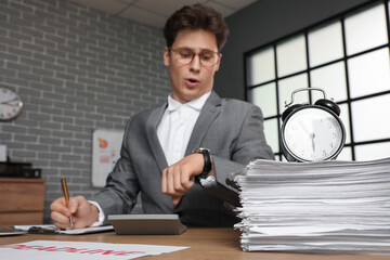 Alarm clock with papers on table against stressed businessman trying to meet deadline in office,...