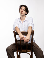 Attractive teenage boy posing on chair in studio over white background.