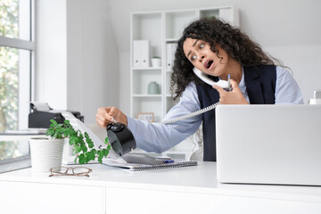 Young African-American businesswoman with alarm clock talking by telephone and trying to meet...