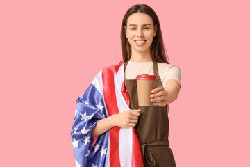 Young female barista with USA flag and cup of coffee on pink background