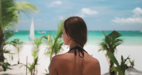 A woman stands on the sandy shore of Boracay Islands White Beach, gazing out at the vast ocean ahead of her.