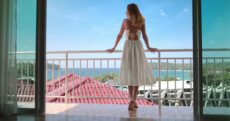 Beautiful happy woman in long dress enjoy ocean view from balcony window door terrace. Female...