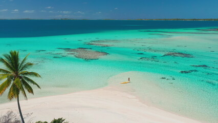Fototapeta premium Aerial drone footage of a woman enjoying a sunny day on a tropical island with a yellow kayak, turquoise water, and a white sand beach