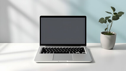 Fototapeta premium A silver laptop with a dark screen sits on a white desk next to a small potted plant. Soft light casts shadows. Minimalist aesthetic.