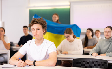 Students study in classroom, teacher stands behind with flag of Ukraine