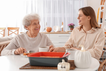 Young woman and her grandmother with tea drinking tasty pie at table in kitchen