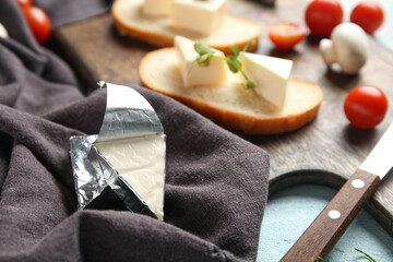 Wooden board with bread, triangles of tasty processed cheese and vegetables on table, closeup