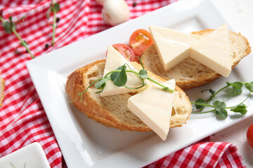 Plate with triangles of tasty processed cheese, bread and micro green on checkered napkin, closeup