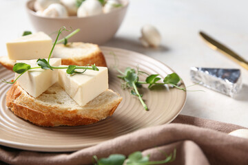 Plate with bread, triangles of tasty processed cheese, micro green and napkin on light table, closeup