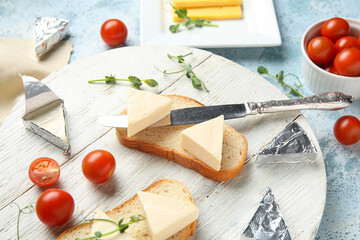 Wooden board with bread, triangles of tasty processed cheese, tomatoes and micro green on color grunge table, closeup