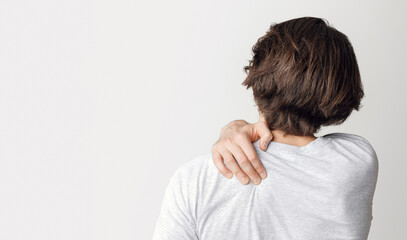 Fototapeta premium Pain in back and shoulder from working at computer. Man presses his hand to sore spot, isolated on gray background, studio shot