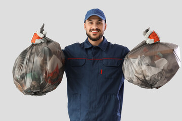 Male scavenger with full garbage bags on light background