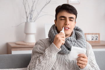 Ill young man with nasal drops at home, closeup