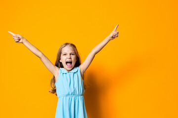 Little girl in blue dress joyfully raising her hands against a vibrant orange background