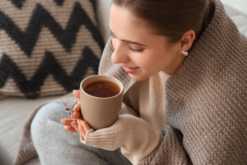 Ill young woman with plaid drinking lemon tea on sofa at home, closeup