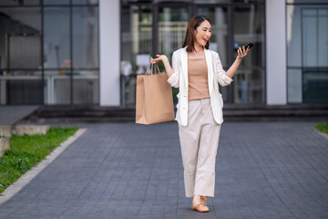 A woman is walking down a sidewalk with a shopping bag in her hand