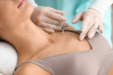Young woman receiving injection in her chest on couch at cosmetologist's office, closeup